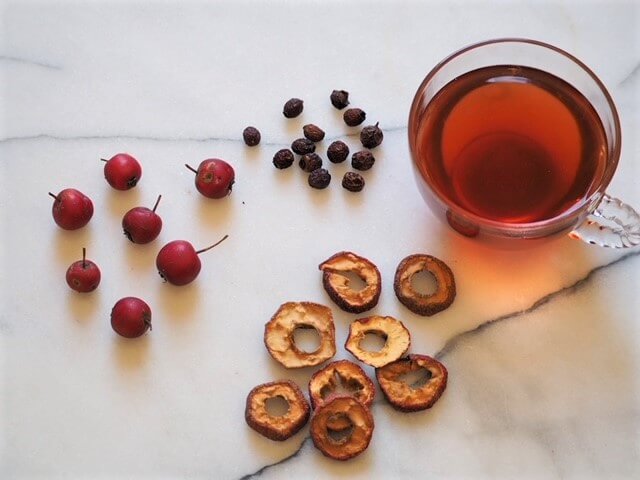 photo of fresh and dried berries with cup of hawthorn berry tea on white marble
