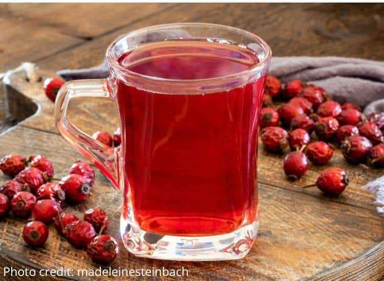 photo of rosehip tea in glass mug with whole rosehips on wooden table