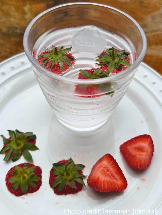 photo of glass with sparkling water with strawberry tops floating in it