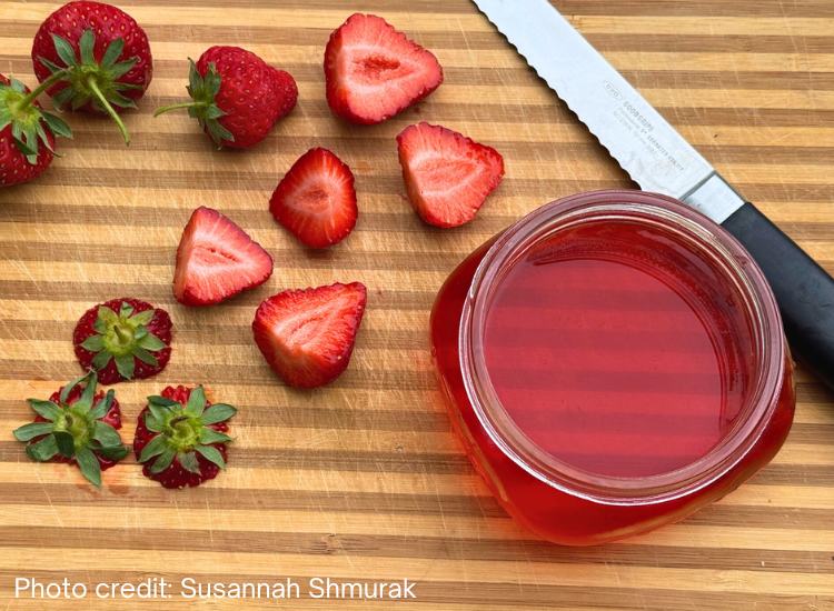 photo of glass jar fillled with strawberry top vinegar on cutting board with cut strawberries and tops