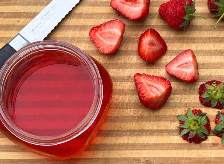 photo of jar of infused vinegar made with strawberry tops on cutting board with cut strawberries and knife