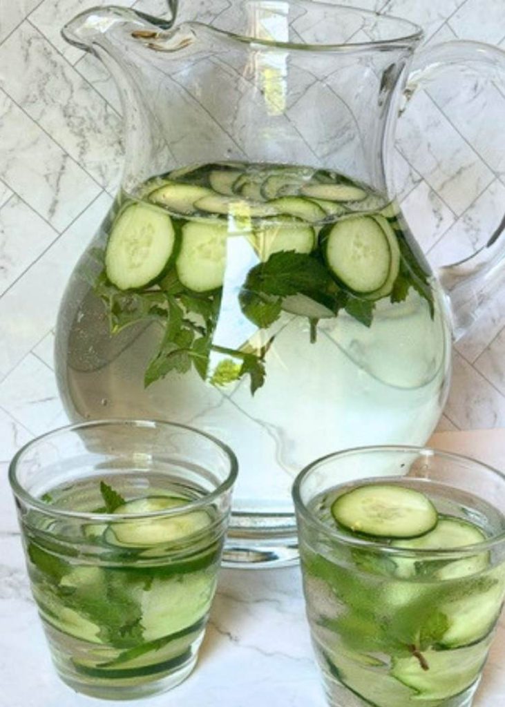 photo of cucumber water with mint in glass pitcher and two glasses on white marble background